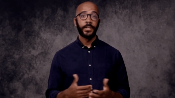 Screenshot of Crash Course's Clint Smith, wearing a button-down shirt and speaking in front of a gray background. 