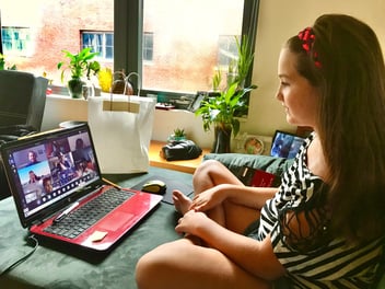 A young girl with a red laptop sits on a microfiber couch in her home, participating in a Zoom call for school. Photo by Maria Thalassinou.