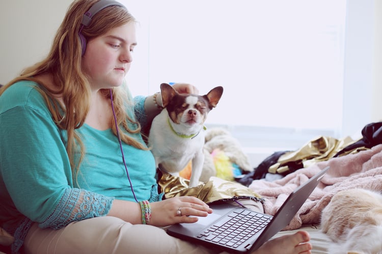 A 19-year-old woman with Autism and other learning disabilities petting her dog and using her laptop at home for school.