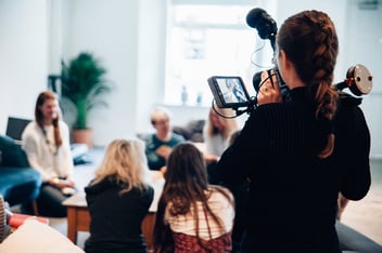 A woman records a video of a group of people, who are gathered around a table.