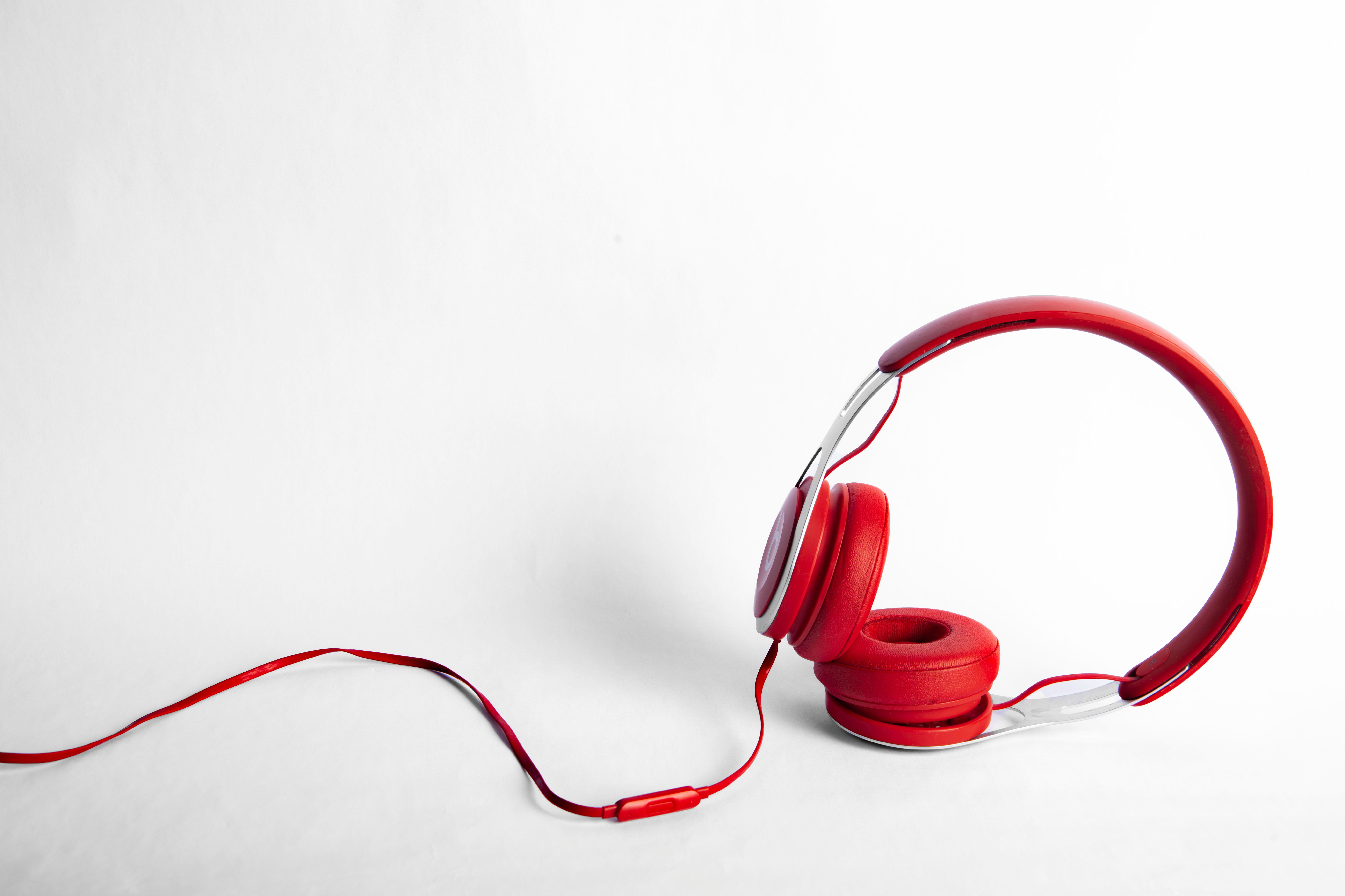 Red and silver headphones with a red wire, propped up on an all-white surface